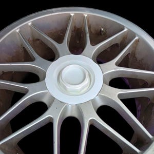 Può includere: Un cerchio per auto in lega argentata con un coprimozzo bianco e una valvola argentata. Il cerchio ha 10 raggi.