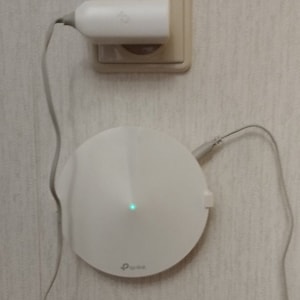 May include: A white, round TP-Link router with a green light on the front, plugged into a white wall outlet.