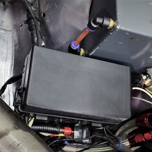 Pode incluir: Uma visão de perto do compartimento do motor de um carro, mostrando uma caixa elétrica preta, um reservatório de fluido cinza com uma tampa amarela, um filtro de óleo preto e várias mangueiras e fios.