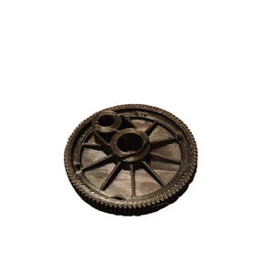 May include: A black plastic gear with a toothed edge and a central hub with two smaller gears. The gear has a radial pattern of spokes.