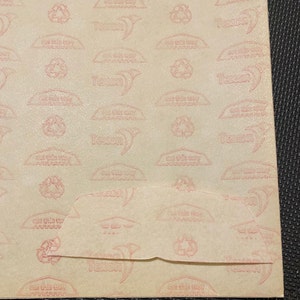 Pode incluir: Um close-up de um papel bege com um padr&atilde;o repetitivo de texto e s&iacute;mbolos rosa. O texto inclui "cut this way" e o nome da marca "Texon". Um s&iacute;mbolo de reciclagem tamb&eacute;m est&aacute; presente. O papel est&aacute; dobrado na parte inferior.
