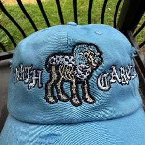 May include: Light blue baseball cap with distressed details. Features an embroidered ram graphic and the words "NORTH CAROLINA" in white. A stylish accessory for fans of the state.