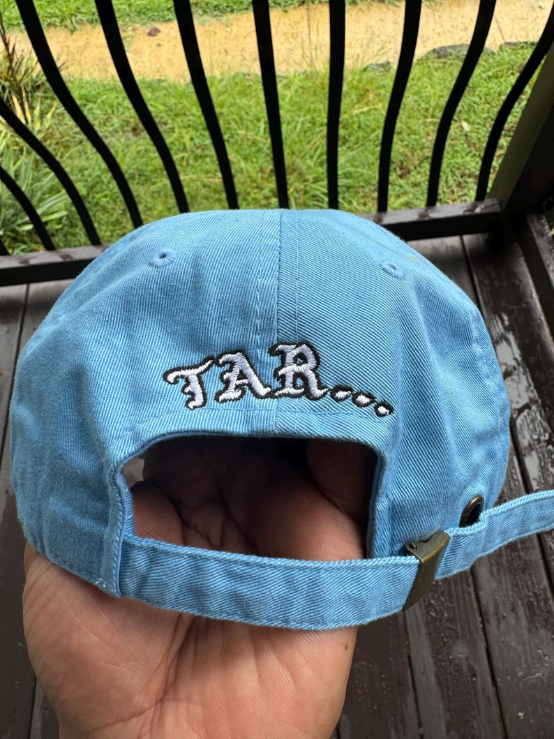 May include: Light blue baseball cap with the word "TAR..." embroidered in white. The cap has a curved brim and an adjustable strap with a metal buckle. The cap is made of a soft, durable fabric.