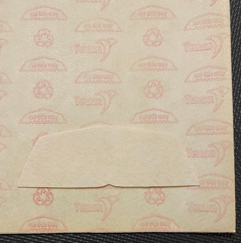 Pode incluir: Close-up de um papel bege claro texturizado com um padr&atilde;o repetido de texto e s&iacute;mbolos rosa. Uma se&ccedil;&atilde;o do papel &eacute; recortada, revelando uma camada bege mais clara por baixo. O texto inclui a palavra "Texon" e "cut this way."