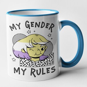 May include: White ceramic mug with a blue rim and handle. The mug features a cartoon illustration of a person with a yellow, white, and purple hairstyle. The text "MY GENDER MY RULES" is printed on the mug.