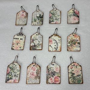 May include: Twelve rectangular paper tags with scalloped tops and metal wire loops. Each tag features a unique collage design incorporating vintage-style floral patterns, botanical illustrations, clock faces, and printed text in black and cream.