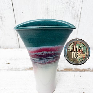 May include: A teal, white, and pink ceramic vase with a wide, flared opening. The vase has a unique, hand-painted design with streaks of color.