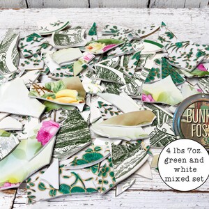 May include: A collection of broken ceramic shards featuring green and white patterns, floral motifs, and landscape illustrations. The set weighs 4 lbs 7 oz and includes various fragments with printed text and colorful accents on a white base.
