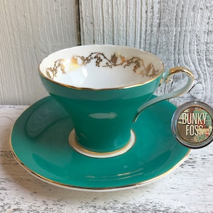 May include: A teal teacup and saucer set with a gold trim and floral design. The cup has a white interior and a flared shape.