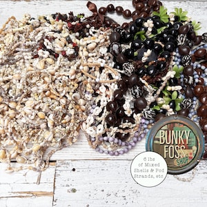 May include: A collection of 6 pounds of mixed shells and pod strands, including brown, black, and white beads. The image also includes a sign that reads "Bunky Foss Shop".