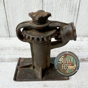 May include: A vintage rusty metal car jack with a gear mechanism and a square base. The jack is in good condition and has a worn, aged look.
