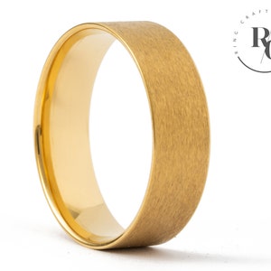 May include: A gold-coloured brushed finish wedding band. The band is thick and has a rounded edge.