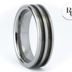 Può includere: Un anello in carburo di tungsteno argentato con due intarsi in fibra di carbonio nera. L'anello ha un bordo smussato e una finitura lucida.