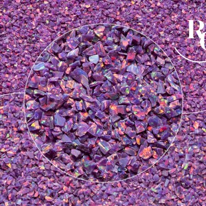 May include: Close-up of a pile of crushed purple opal gemstones. The stones have a rough, irregular texture and display flashes of iridescent colour. The gemstones are suitable for jewellery making and other crafts.