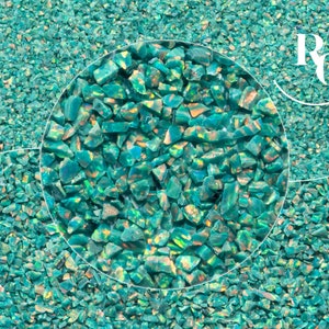 May include: Close-up of teal blue iridescent opal gemstone chips. The chips are small and irregular in shape, with a shimmering, pearlescent finish.
