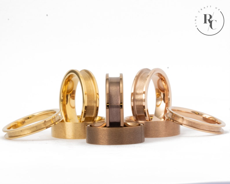 May include: A set of six wedding bands in different colours, including gold, rose gold, and a darker metal. The bands are all polished and have a bevelled edge.
