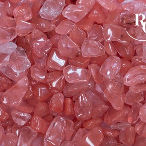 May include: A close-up view of a pile of pink rose quartz tumbled stones. The stones are smooth and polished, with a translucent appearance.