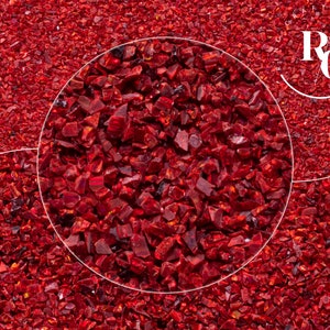 Puede incluir: Primer plano de trozos de vidrio rojo oscuro triturados. Los fragmentos tienen forma irregular y reflejan la luz, creando un efecto brillante. La imagen está llena de vidrio rojo, con una incrustación circular que muestra una vista ampliada.