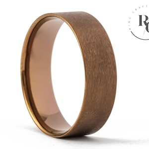 May include: A brushed gold wedding band with a rounded edge. The band is made of tungsten carbide and has a matte finish.