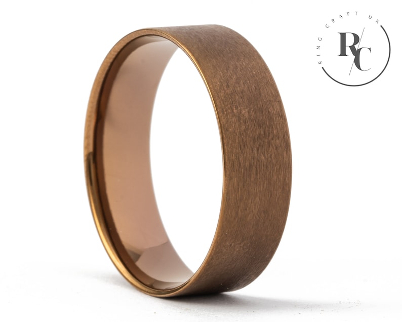 May include: A brushed gold wedding band with a rounded edge. The band is made of tungsten carbide and has a matte finish.