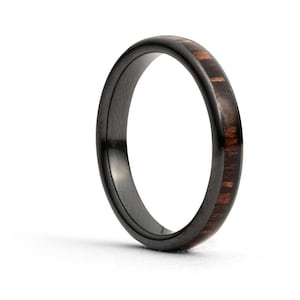 Puede incluir: Un anillo de cerámica negra con una fina banda de incrustación de madera oscura.