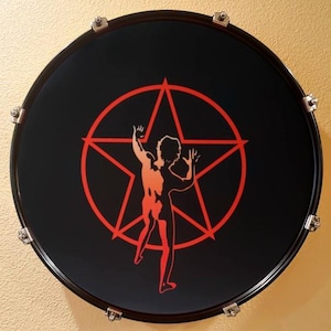 May include: A black drumhead featuring a red star and a stylized human figure. The drumhead has a black rim and silver hardware. The design is a graphic illustration.