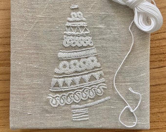 May include: A white embroidered Christmas tree design on a beige linen canvas with white embroidery floss.