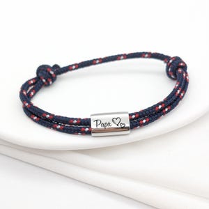 Pu&ograve; includere: Un braccialetto in corda blu e rosso con un ciondolo d'argento che dice "Pap&agrave;" con due cuori.
