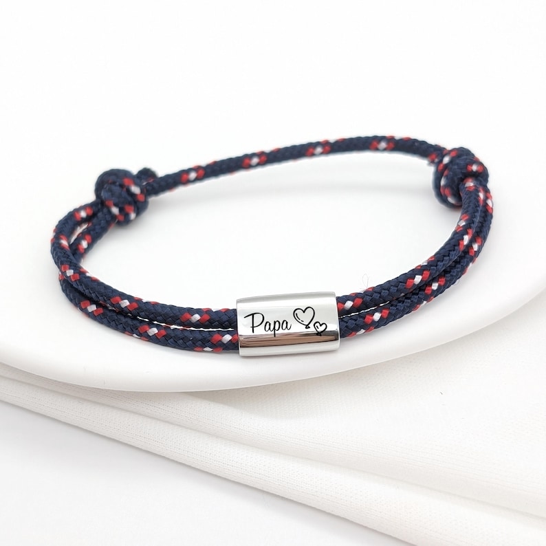 Pu&ograve; includere: Un braccialetto in corda blu e rosso con un ciondolo d'argento che dice "Pap&agrave;" con due cuori.