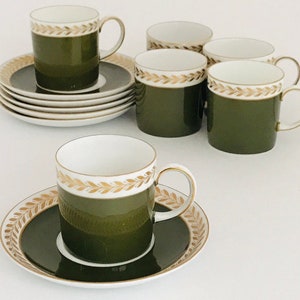 May include: A set of olive green and white ceramic teacups and saucers. The cups have a gold leaf pattern around the rim and a matching design on the saucers. The set includes multiple cups and saucers, perfect for serving tea or coffee.