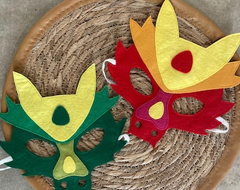 May include: Two felt dragon masks. One is green and yellow, the other is red, yellow, and orange. Each mask has eye holes and white elastic bands. The masks are on a round woven mat.