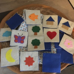 Peut inclure: Un ensemble de carrés en feutre avec différentes images, dont un poisson, une maison, un arbre, un cœur, une fleur, un papillon, une lune, une étoile et un nuage. Les carrés sont disposés en cercle sur un panier en osier.