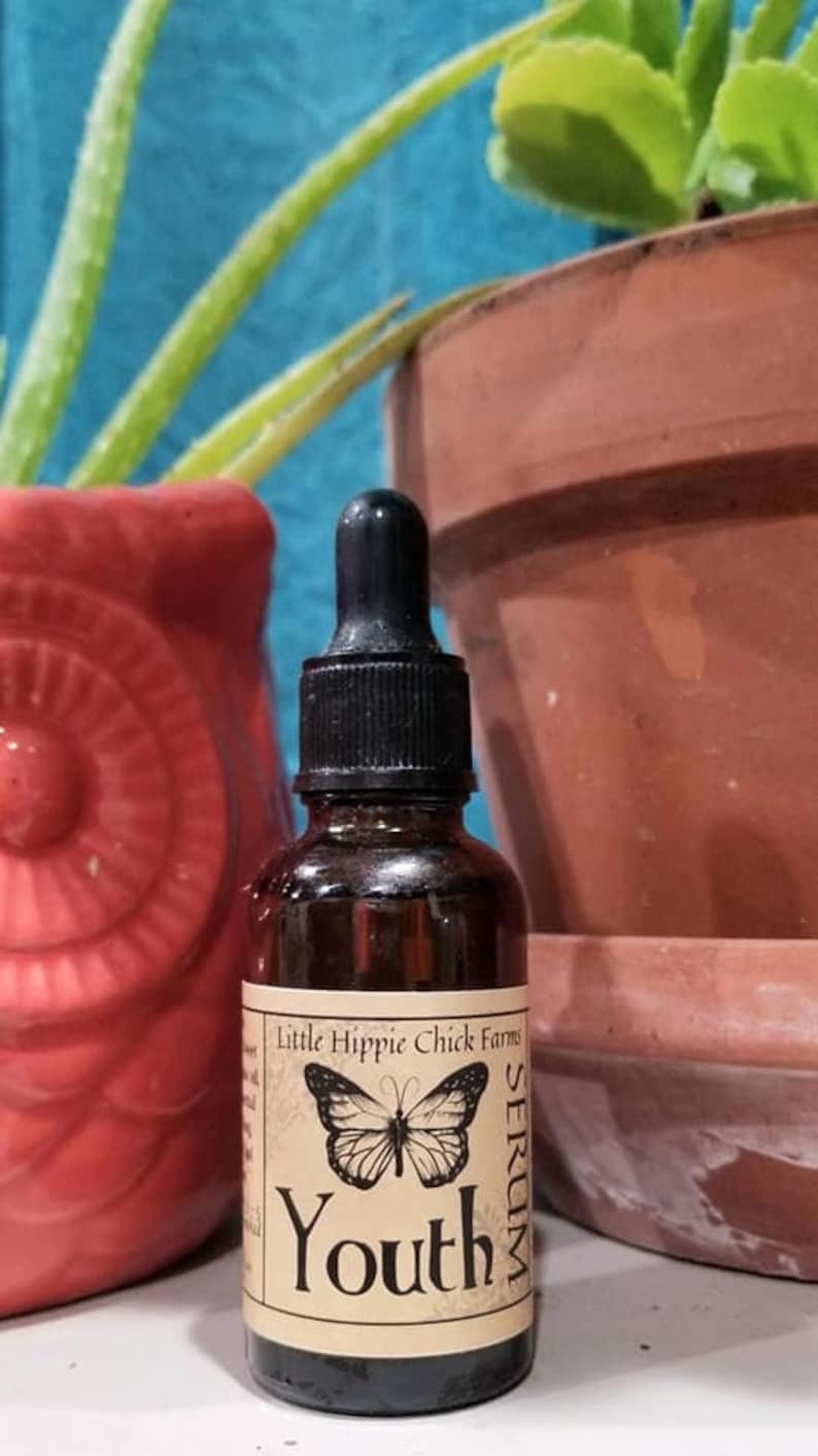 May include: A brown glass bottle with a black dropper top and a label that reads "Little Hippie Chick Farms Serum Youth". The label features a black butterfly graphic.