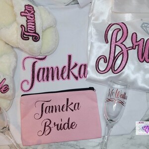 May include: A bridal robe, slippers, makeup bag, and champagne flute, all personalized with the name "Tameka" and the word "Bride" in pink glitter lettering.