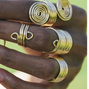 May include: A set of four gold-toned rings, each with a unique design. The rings are stacked on a finger, creating a bold and stylish look.