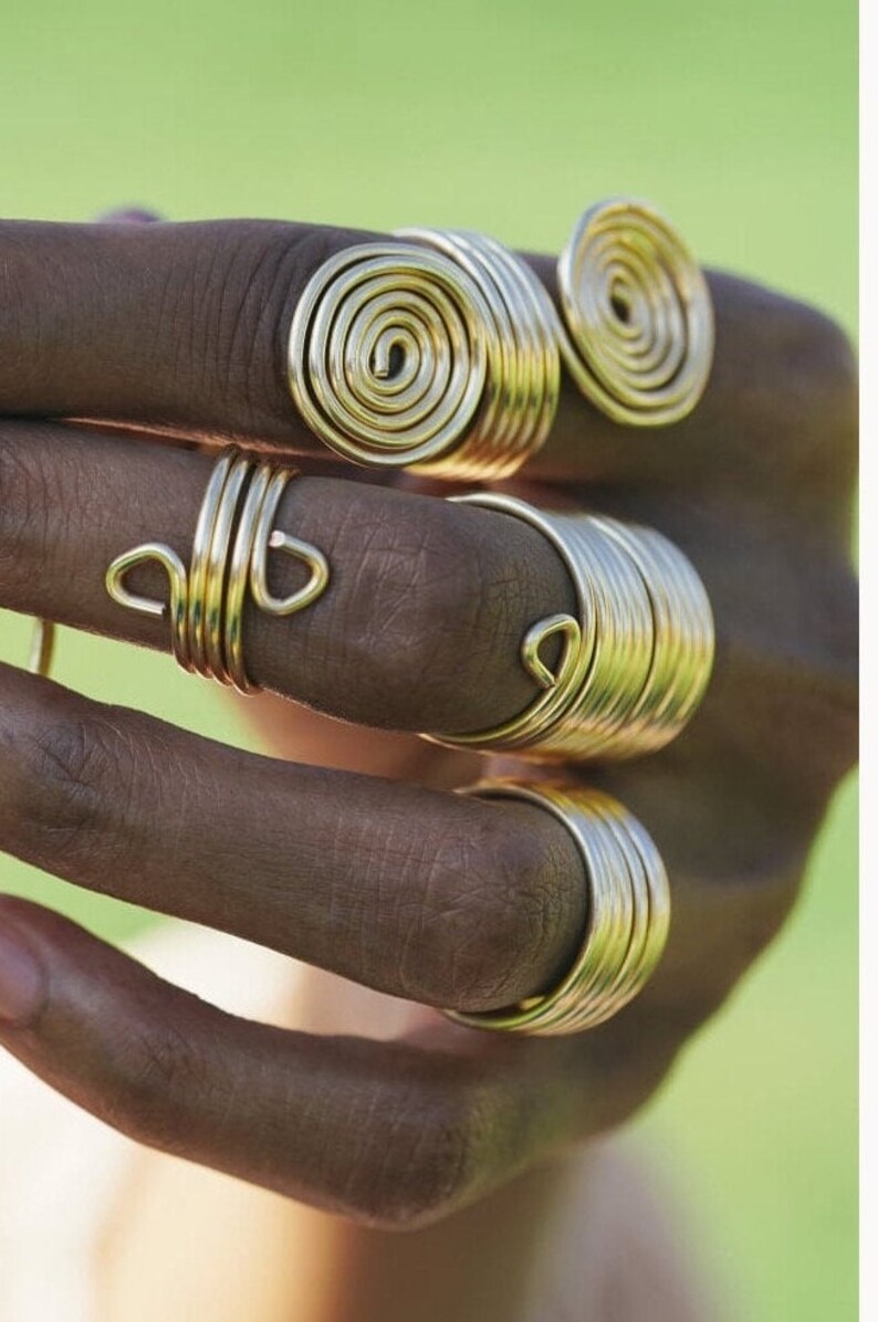 May include: A set of four gold-toned rings, each with a unique design. The rings are stacked on a finger, creating a bold and stylish look.