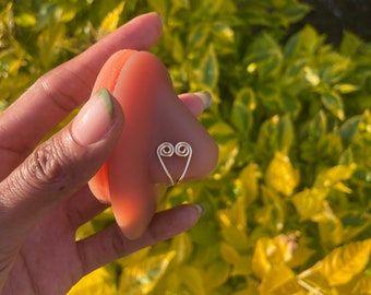 May include: A gold heart-shaped ring with a double-loop design. The ring is held in a hand with manicured nails.