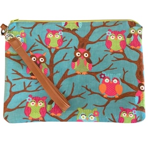 May include: A teal clutch with a brown leather wrist strap. The clutch features a repeating pattern of colorful owls perched on brown tree branches. The owls are in shades of pink, green, orange, and brown.