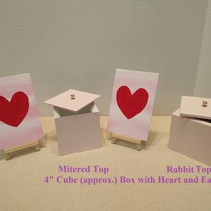 May include: Three pink wooden boxes with a heart design. The boxes are 4 inches in size and have a mitered top or a rabbit top. The boxes are on small wooden easels.