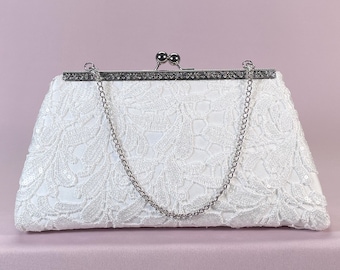 May include: White lace clutch with a silver chain and a silver clasp. The clutch has a floral design.