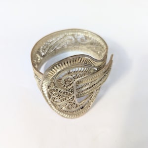 May include: A silver filigree ring with a delicate, intricate design. The ring is open and has a unique, curved shape.