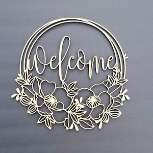 May include: A white wooden welcome sign with a floral wreath design. The sign is in the shape of a circle and has the word "welcome" written in a cursive font.