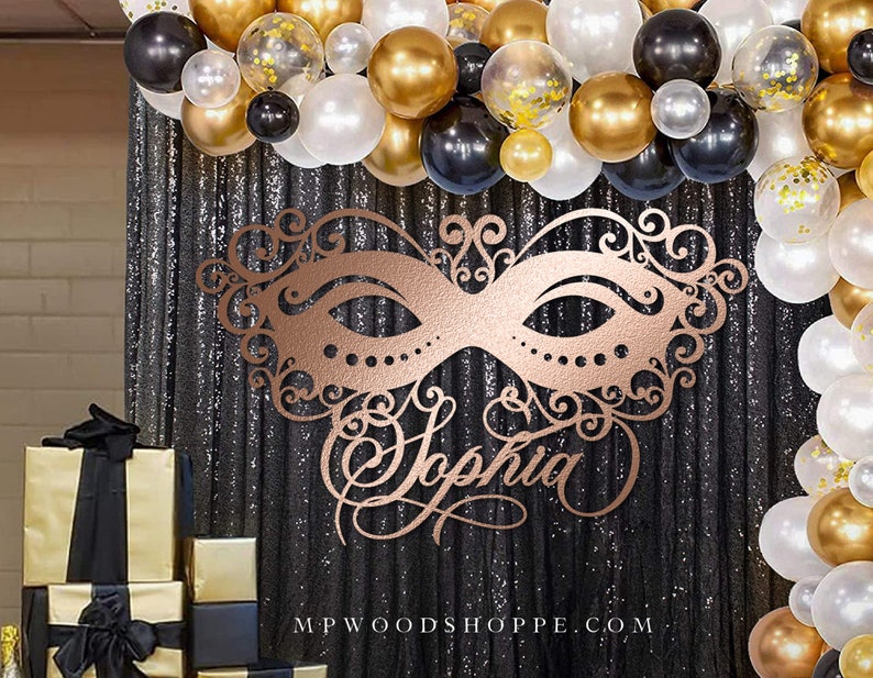 K&ouml;nnte beinhalten: Eine ros&eacute;goldene Maskenballmaske mit filigranen Details und dem Namen "Sophia" in dekorativer Schrift. Die Maske wird vor einem schwarzen Paillettenhintergrund mit einem Ballonbogen aus schwarzen, goldenen und wei&szlig;en Ballons pr&auml;sentiert.
