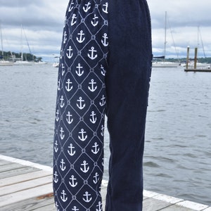 May include: Navy blue terry cloth pants with a white anchor and rope pattern on one leg. The pants are shown on a wooden dock with a body of water in the background.