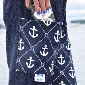 May include: A navy blue towel with a large pocket featuring a white anchor pattern. The pocket has a smaller label with the text "Paradise" and a palm tree logo. The towel has a white label with the text "Since 1982".