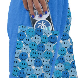 May include: Blue terry cloth shorts with a large pocket on the side. The pocket is lined with a white background and a pattern of blue smiley faces. The shorts have a white label with the text "Paradise" and a palm tree logo.