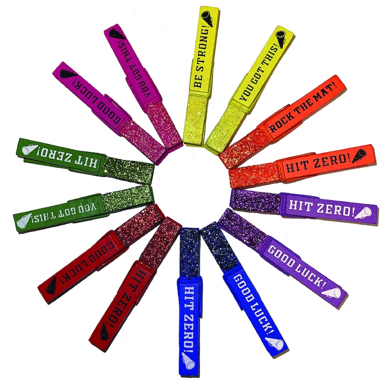 May include: A set of 14 colorful glitter clothespins with motivational phrases like "Hit Zero!" and "Good Luck!" printed on them. The clothespins are arranged in a circle.