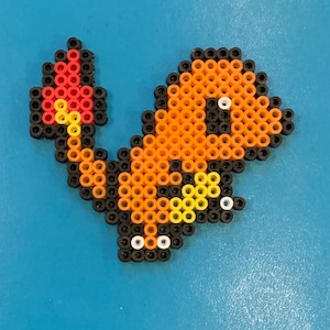 May include: A pixel art design of a Pokemon character, Charmander, made with colorful beads. The character is orange and yellow with black outlines and white eyes. The tail is a flame with red, orange, and yellow beads.