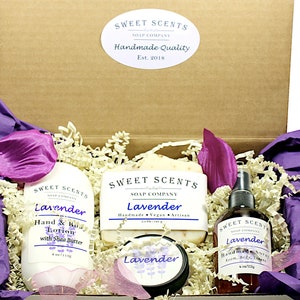 May include: A gift box filled with lavender-scented bath and body products. The box contains a bottle of hand and body lotion, a bar of soap, a jar of body butter, and a bottle of room spray. All products are labeled "Sweet Scents" and "Lavender".