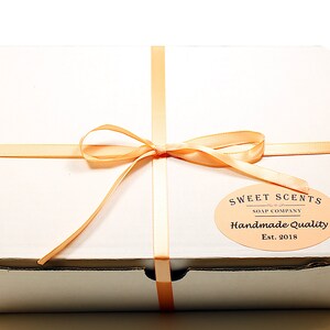 May include: A white gift box with a peach-colored ribbon tied in a bow. The box has a label that reads "Sweet Scents Soap Company Handmade Quality Est. 2018."